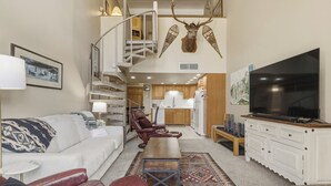 Ein modernes Wohnzimmer mit einer Couch, einem Couchtisch, einem Fernseher, einem Kamin und einer Treppe zu einer oberen Ebene.