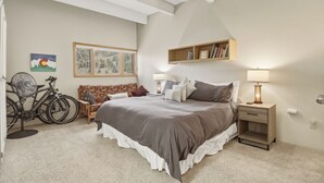 Ein Schlafzimmer mit einem großen Bett, einem Nachttisch mit Lampe, einem Bücherregal, einem Fahrrad und einem Bild an der Wand.