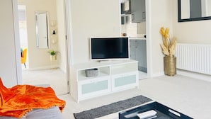 A modern living room with a flat-screen TV, white entertainment unit, and a large mirror. - Amber 1BR Apart 14 min Walk to Tattersalls (Newmarket)