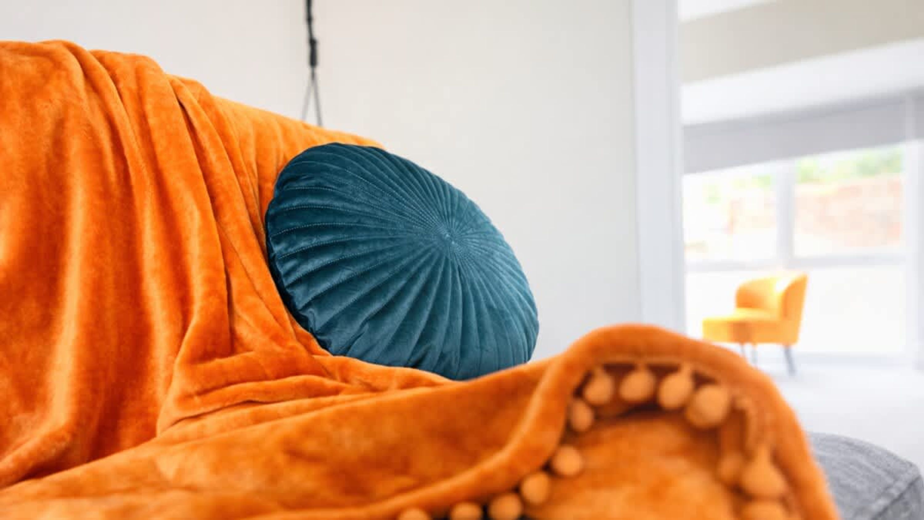 A room with a large window, a bright yellow chair, and a blanket with a textured pillow.
