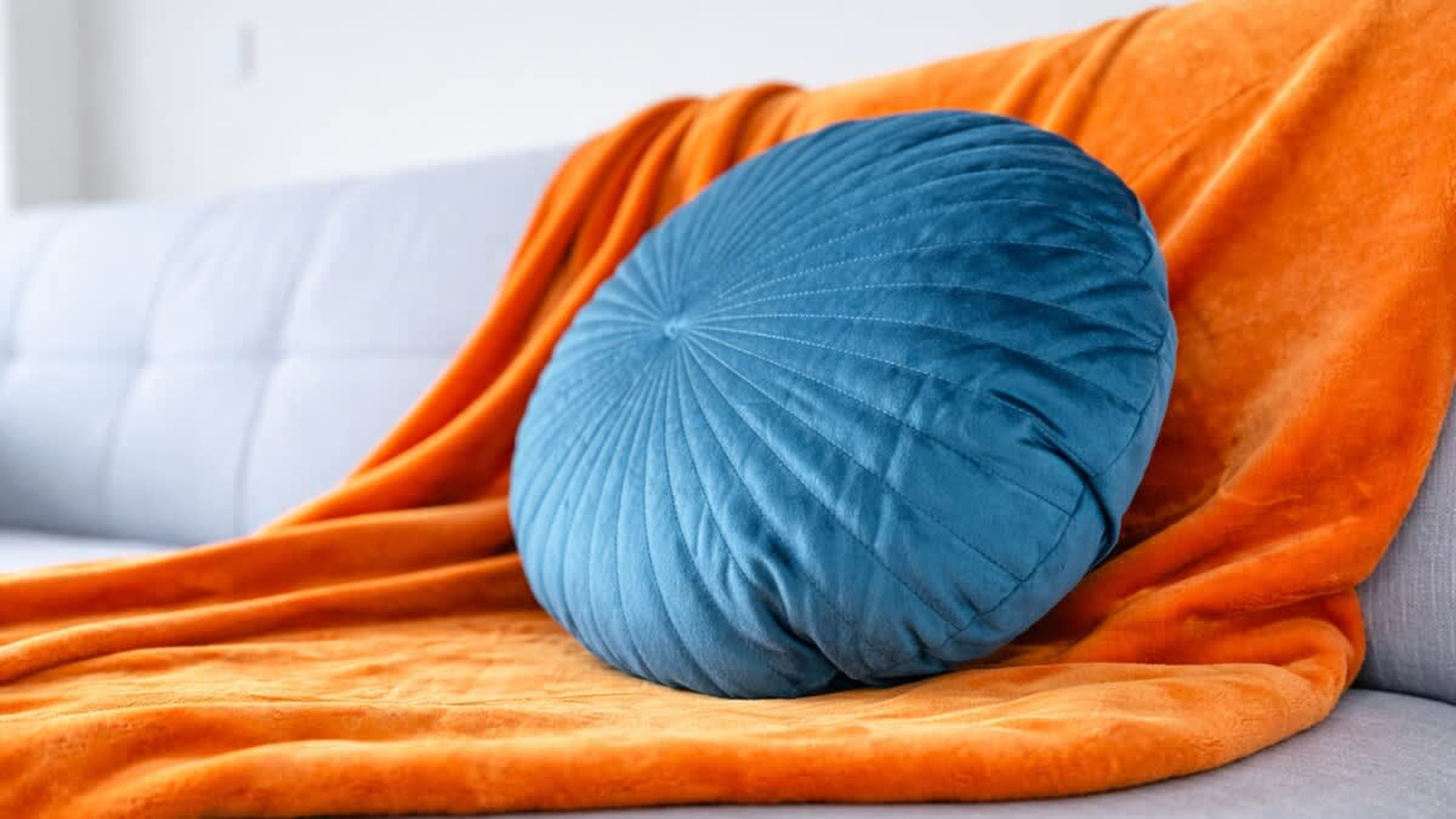 Un coussin bleu sur un canapé, avec une couverture orange.