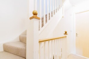 Un escalier dont les marches sont recouvertes d’un tapis beige, avec des rampes blanches et des balustres en bois.