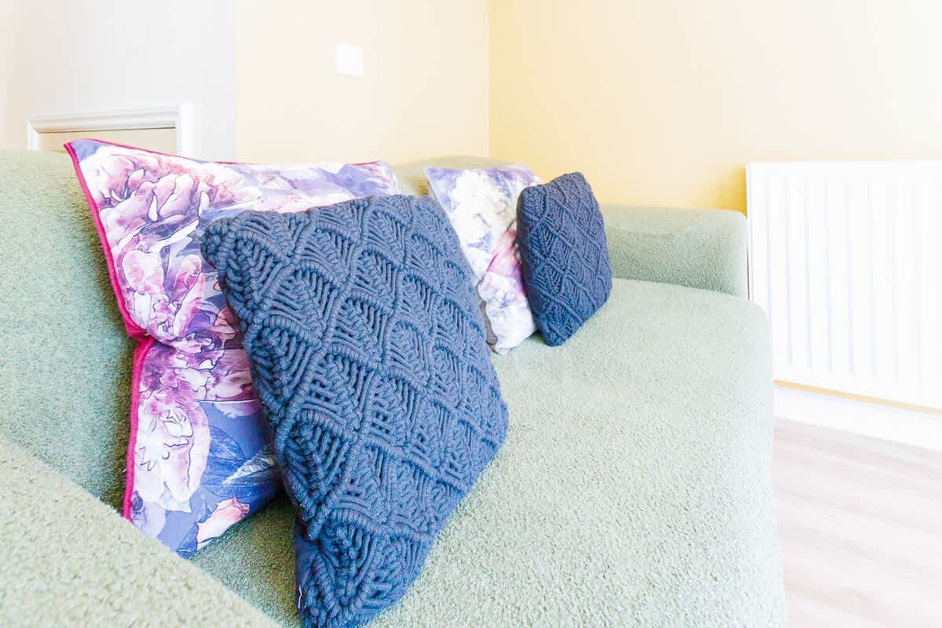 Ein Sofa mit blumigen und strukturierten Kissen, einer grünen Decke und einem weißen Heizkörper.