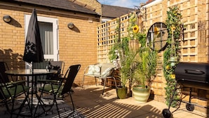 A patio with a table and chairs, a barbecue grill, and a brick wall with a wooden fence. - Riverside GEM 6BR With River View NR City Centre (Cambridge)