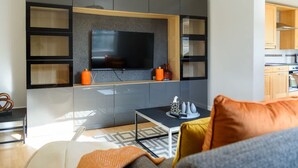 A modern living room with a flat-screen TV mounted on a wall, a coffee table, and a sofa with cushions. - Riverside GEM 6BR With River View NR City Centre (Cambridge)