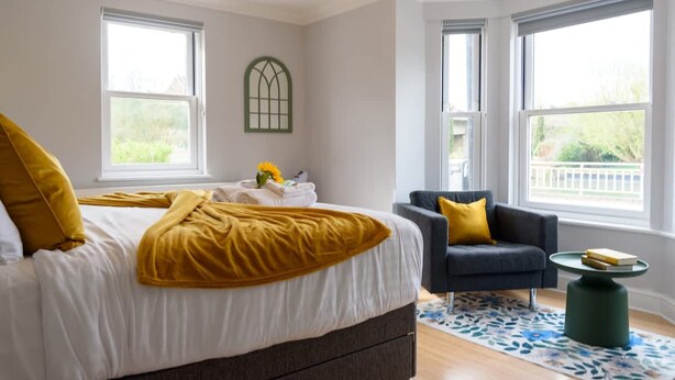A bedroom with a bed, a chair, a table, and large windows. - Riverside GEM 6BR With River View NR City Centre (Cambridge)