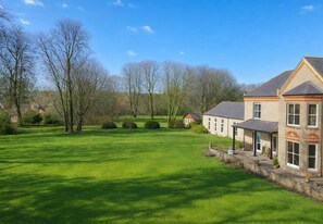 A large, open grassy area with a building featuring a stone facade and multiple windows. - Dettori 2BR With Garden 11 Mins Walk to Gallops (Newmarket)