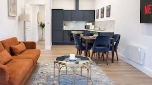 A modern living room with a sofa, a coffee table, and a dining area with chairs and a table. - Dettori 2BR With Garden 11 Mins Walk to Gallops (Newmarket)