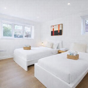 A hotel room with two beds, a window with frosted glass, a wall-mounted abstract painting, and bedside tables with toiletries. - Dettori 2BR With Garden 11 Mins Walk to Gallops (Newmarket)