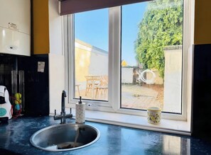 A kitchen with a sink, a window, and a view of a patio with outdoor furniture. - 4 BR House 13 min Walk to Tattersalls Private Garden Parking (Newmarket)