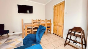 A living room with a blue chair, wooden chairs, a TV, and a wooden door. - 4 BR House 13 min Walk to Tattersalls Private Garden Parking (Newmarket)