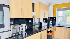 A modern kitchen with wooden cabinets, a black countertop, and stainless steel appliances. - 4 BR House 13 min Walk to Tattersalls Private Garden Parking (Newmarket)