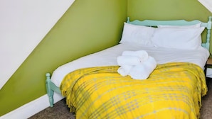 A single bed with a white mattress and pillows, a yellow and grey checkered blanket, and a white towel on the bed. - 4 BR House 13 min Walk to Tattersalls Private Garden Parking (Newmarket)