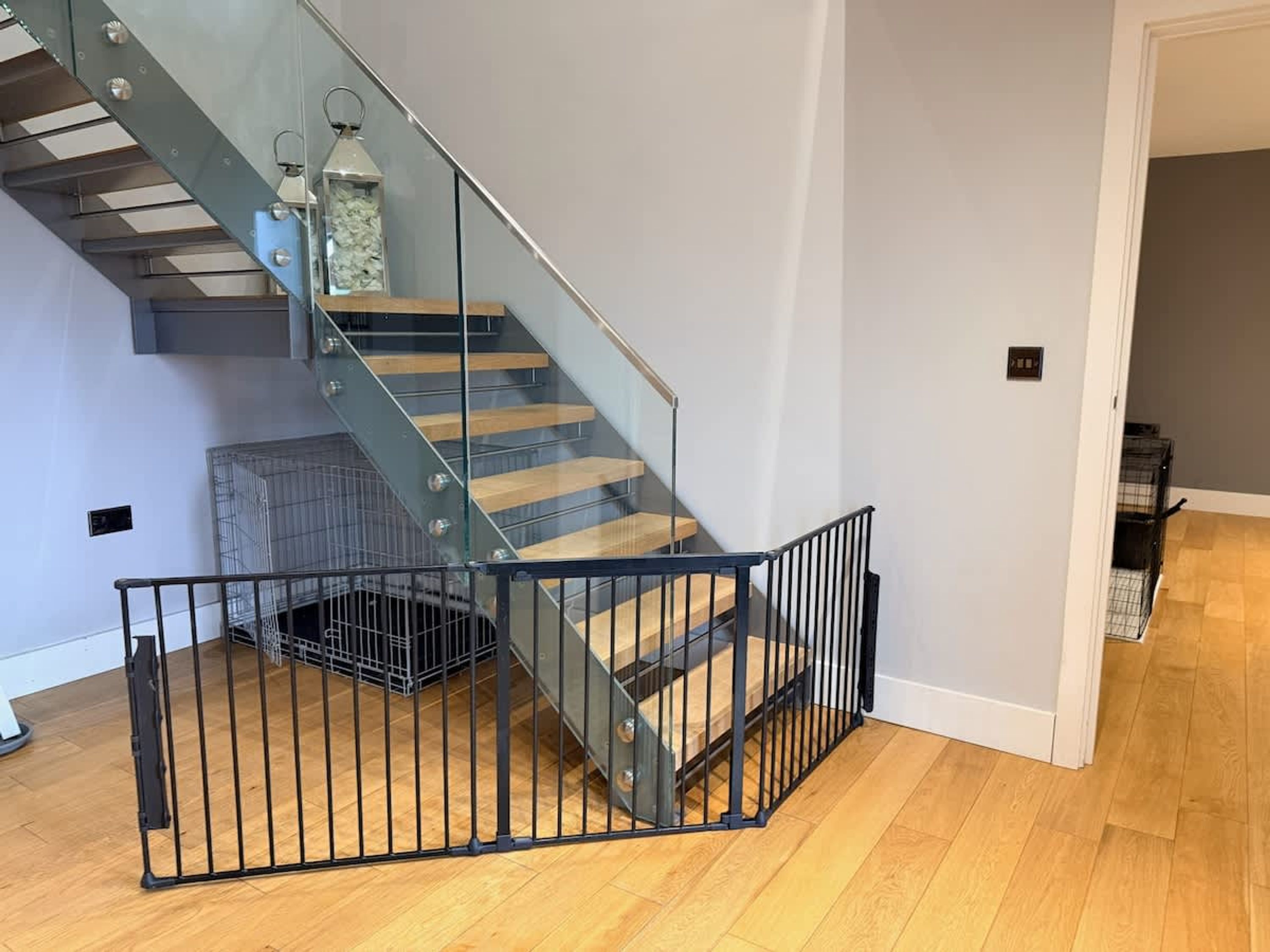 A modern staircase with glass railings, wooden steps, and a metal safety gate.