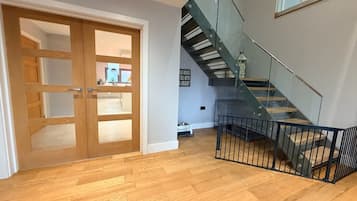 A modern interior with a wooden floor, a glass staircase, and a door leading to another room.