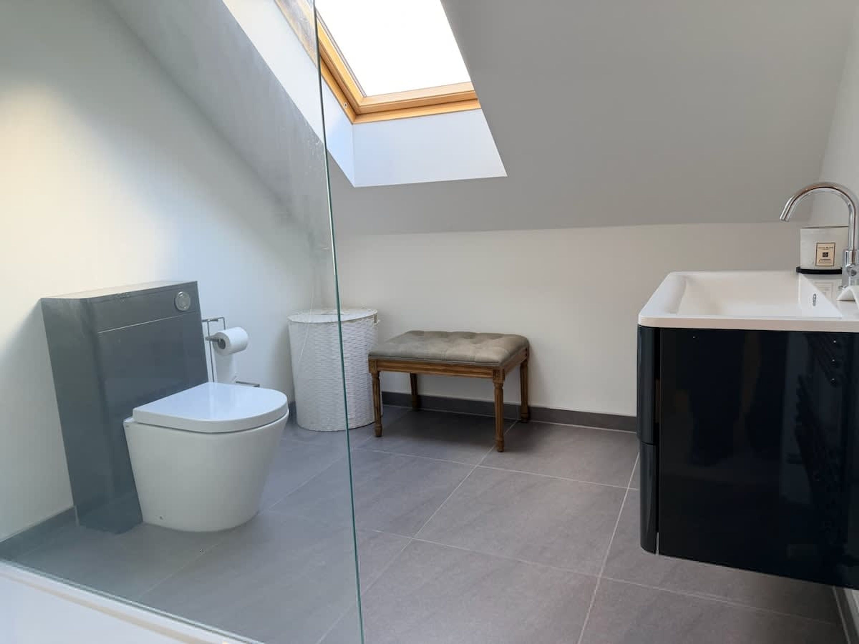A modern bathroom with a skylight, a toilet, a bench, and a sink.