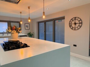Une cuisine moderne dotée d’un îlot central, de luminaires suspendus, d’une horloge et d’un panneau indiquant la sortie de secours.