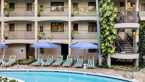 Un hotel con piscina, varios balcones con plantas y sillas de descanso.