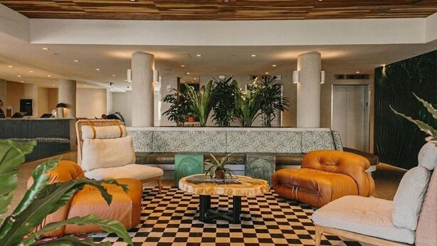 Un vestíbulo con pisos a cuadros, una mesa de recepción, zonas de estar y una planta grande.