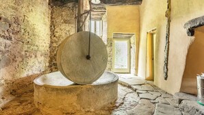 Um moinho de pedra com uma viga de madeira no teto, um interior rústico com soalho de pedra e uma porta que dá para uma área externa.