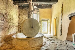 Eine Steingermühle mit einem hölzernen Balken an der Decke, ein rustikaler Innenraum mit Steinboden und eine Tür, die zu einem Außenbereich führt.