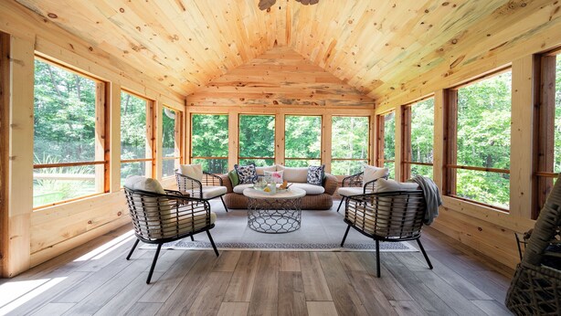 A wooden interior with a high ceiling, large windows, a sofa, two chairs, and a coffee table.