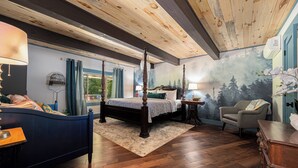 A bedroom with a four-poster bed, a desk with a lamp, a chair, and a mural of a forest on the wall.