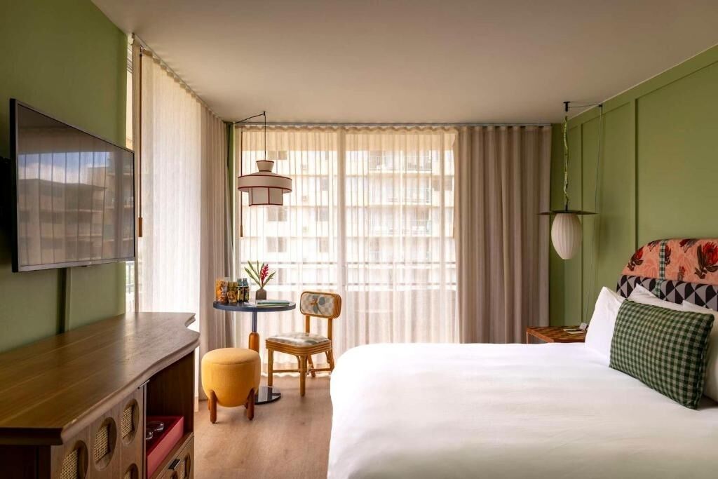 A hotel room with a bed, a desk, a chair, a television, and a window with curtains.