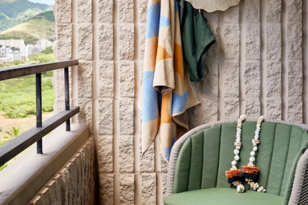 Un balcón con un muro de piedra, una silla verde y una toalla a rayas.