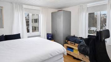 A hotel room with a large bed, wooden flooring, a wardrobe, a desk with a chair, and a window with a view of the outside.