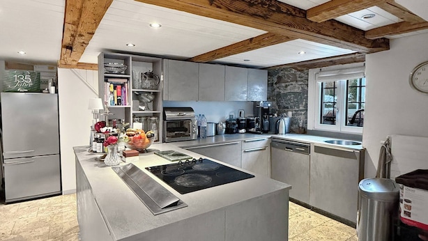 A modern kitchen with a central island, built-in appliances, and a stone accent wall. - Elegant Lake Zurich House With Stunning Views and Private Terrace (Stafa)