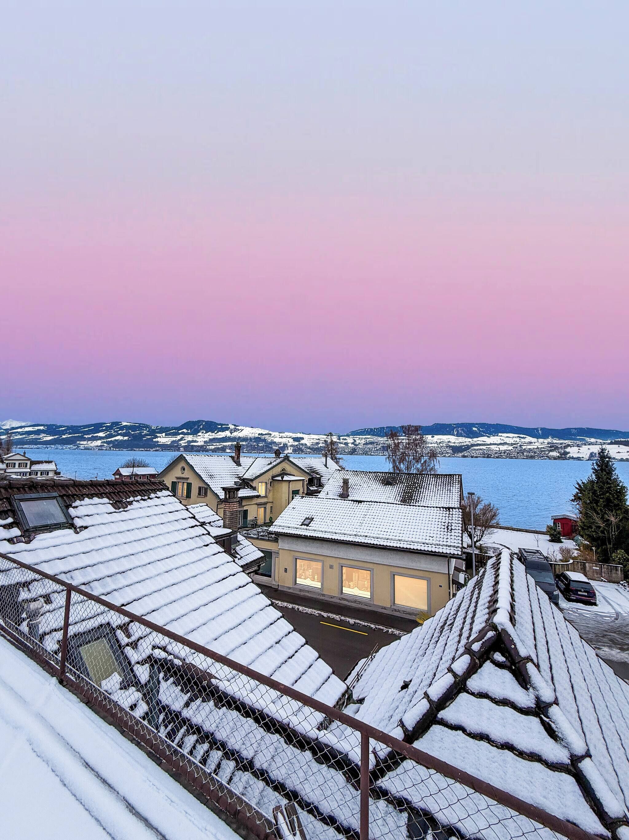 Un quartier résidentiel aux toits enneigés, avec vue sur un lac.