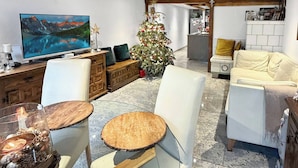 A modern living room with a large flat-screen TV, a wooden dining table, and a Christmas tree. - Elegant Lake Zurich House With Stunning Views and Private Terrace (Stafa)