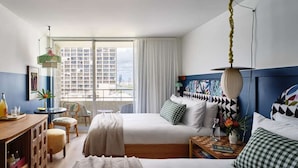 Habitación de hotel con dos camas, un escritorio, una silla, un ventanal con vista a la ciudad y un balcón.