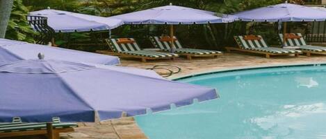 A pool area with lounge chairs and umbrellas, surrounded by greenery.