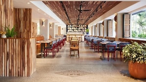 Un restaurante espacioso con mesas largas, paneles de madera y una zona de bar central.