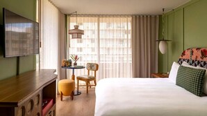 A hotel room with a bed, a desk, a chair, a television, and a window with curtains. - Wayfinder Waikiki | Corner King Lanai | Design Hotel, Saltwater Pool (Honolulu County)