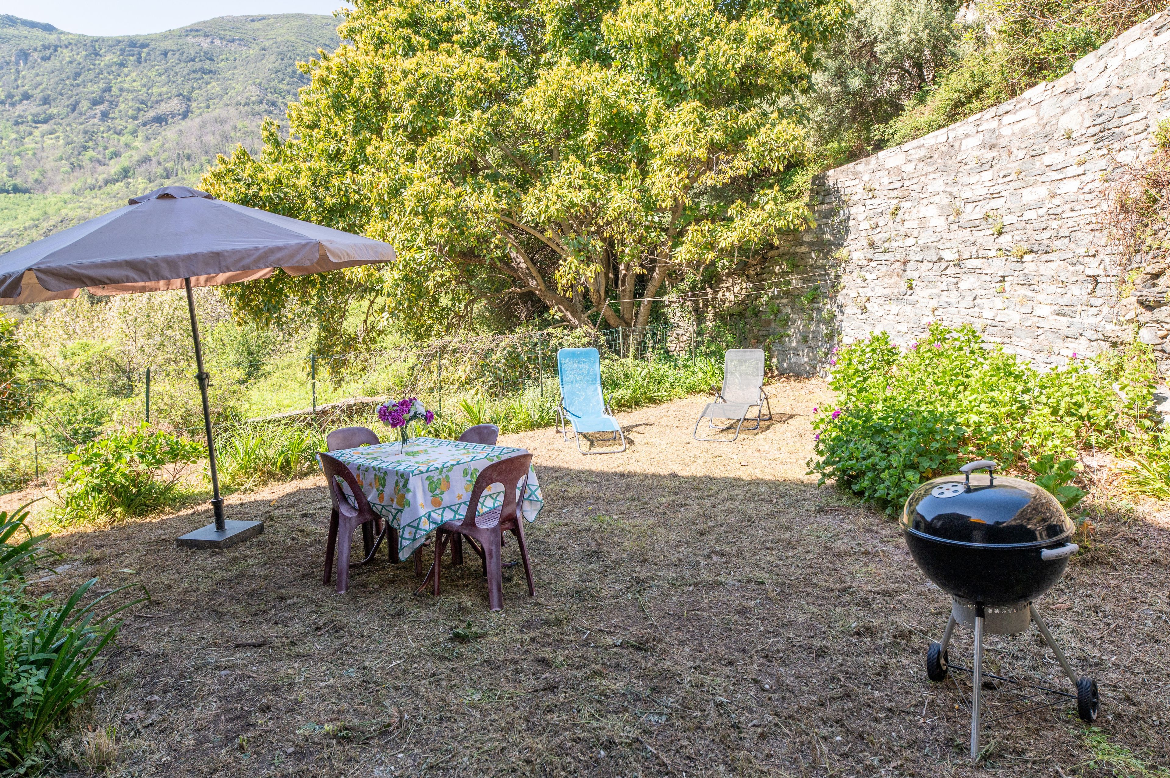 An outdoor dining area with a table and chairs, a barbecue grill, and a stone wall.