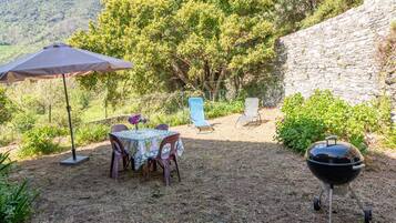 An outdoor dining area with a table and chairs, a barbecue grill, and a stone wall.