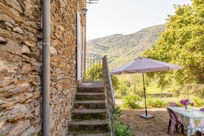 A stone staircase leading to a balcony with a table and umbrella, overlooking a mountainous landscape. - Apartment 'Maisonnette Chez Aurèle' with Mountain View (Santa-Maria-di-Lota)