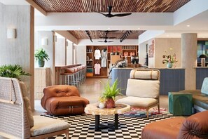Eine moderne Lobby mit Ledersitzmöglichkeiten, einem Schachbrettmuster-Boden und einem Barbereich im Hintergrund.