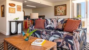 A living room with a sofa, a coffee table, and a bookshelf. - Wayfinder Suite | Wayfinder Waikiki | Waikiki Beach, Saltwater Pool, Kitchen (Honolulu County)