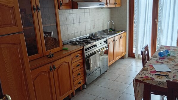 Una cocina con gabinetes de madera, estufa a gas, un lavamanos y una mesa de comedor con mantel floreado.