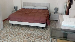 A bedroom with a bed, two bedside tables, a glass table, patterned floor tiles, and a door. - Lilly's house (Avellino)