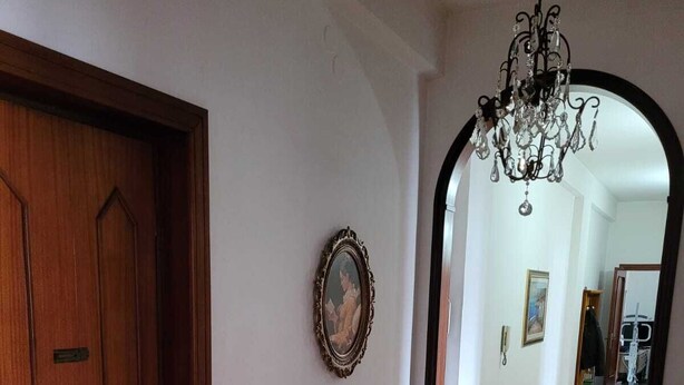 A hallway with patterned floor tiles, a wooden door, a framed picture on the wall, and a chandelier. - Lilly's house (Avellino)