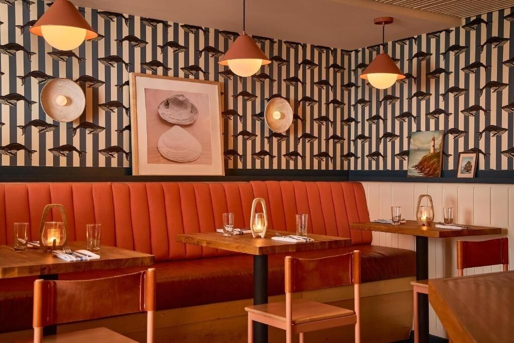 A restaurant interior with striped wallpaper, red seating, and pendant lighting.