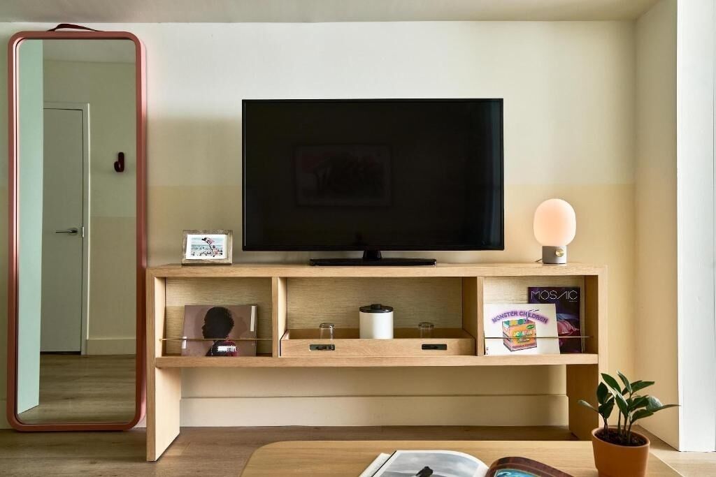 A modern living room with a flat-screen TV on a wooden shelf, a mirror, a small plant, and a framed picture.