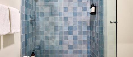 A shower with blue-tiled walls, a wooden bench with towels, and a glass shower door.