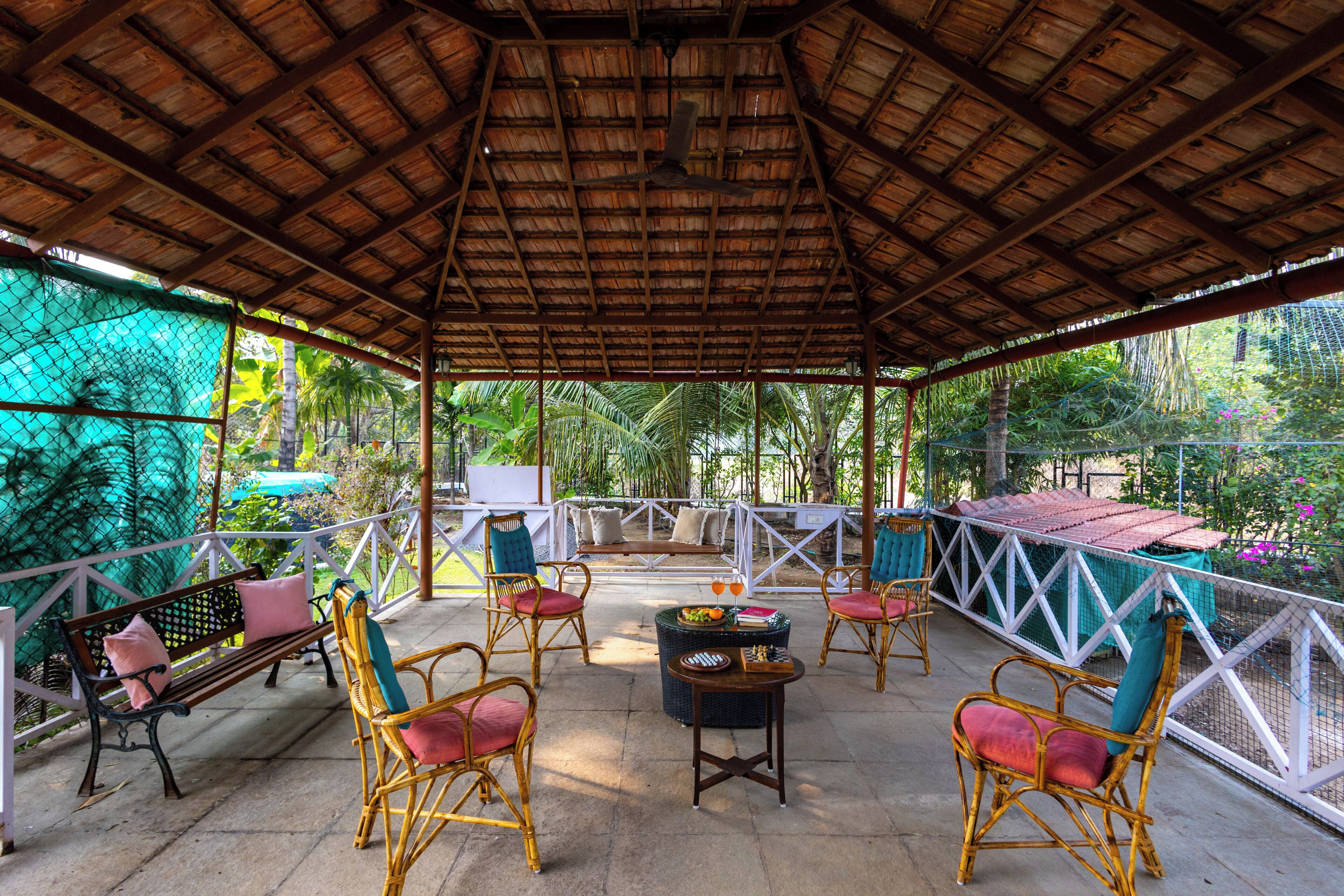 Um pavilhão ao ar livre com telhado de palha, móveis de vime e vista para vegetação tropical.