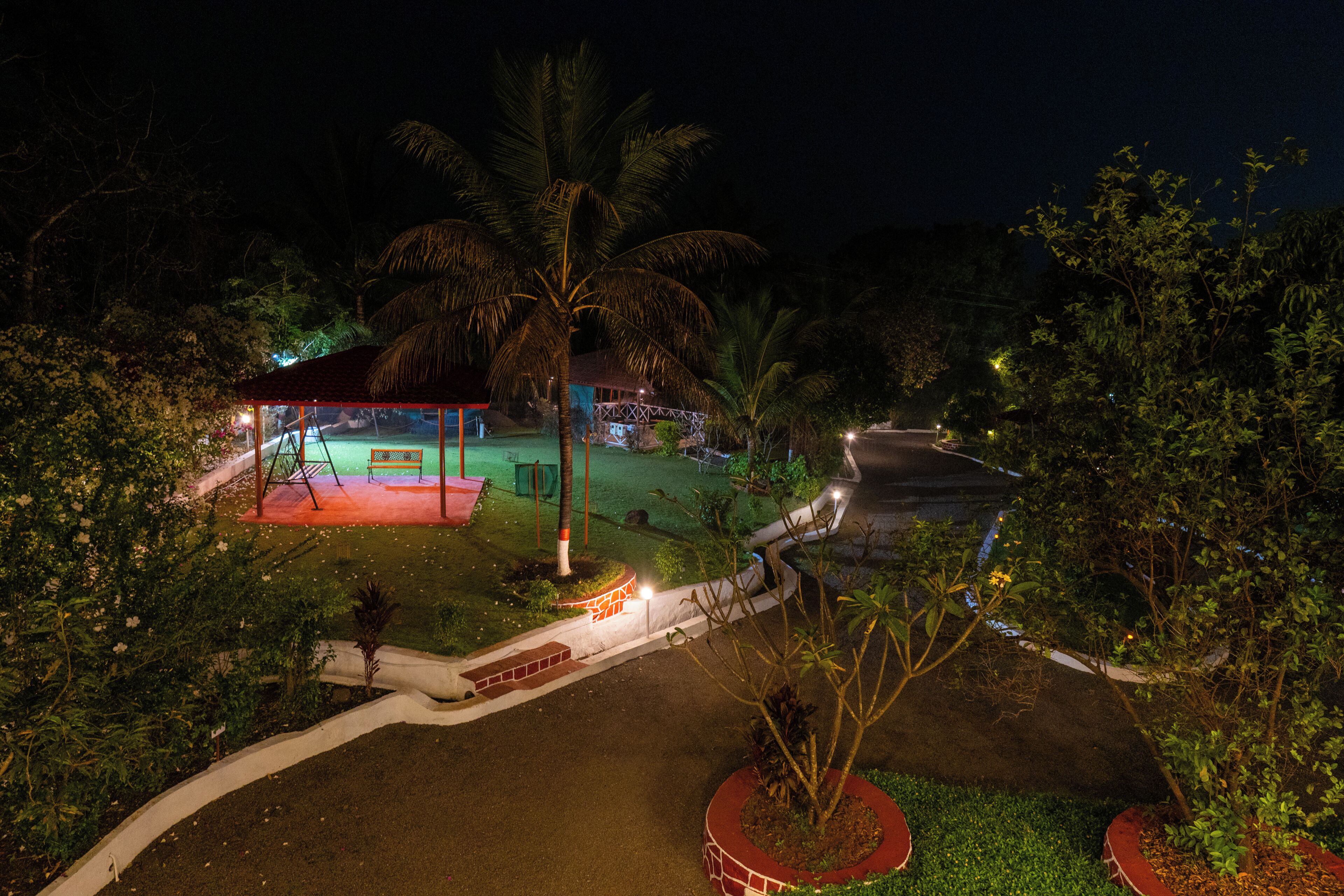 A well-lit outdoor area with a covered seating area, palm trees, and a pathway leading to a building.